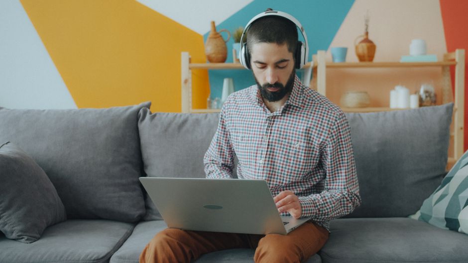 Joven con audífonos trabajando en una laptop desde un sofá